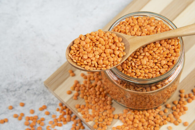 Glass jar of red lentils with wooden spoon on wooden board